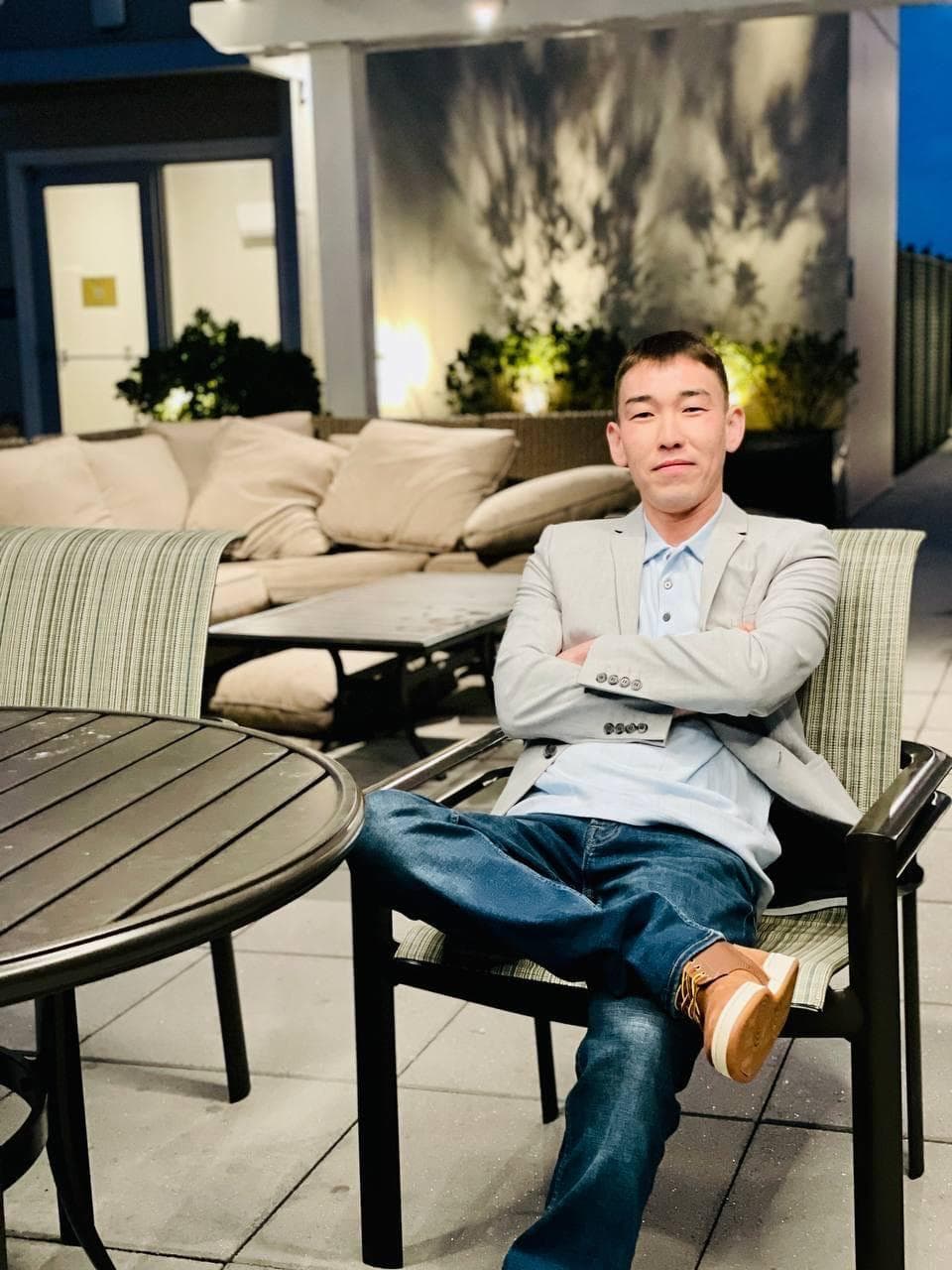 Man in a grey blazer and jeans sits cross-legged on a modern outdoor patio.